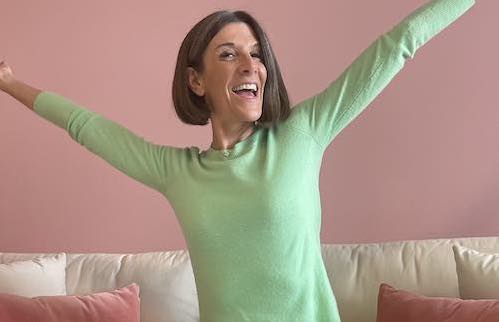 Laura Graye is smiling and sitting in sofa stretching her arms